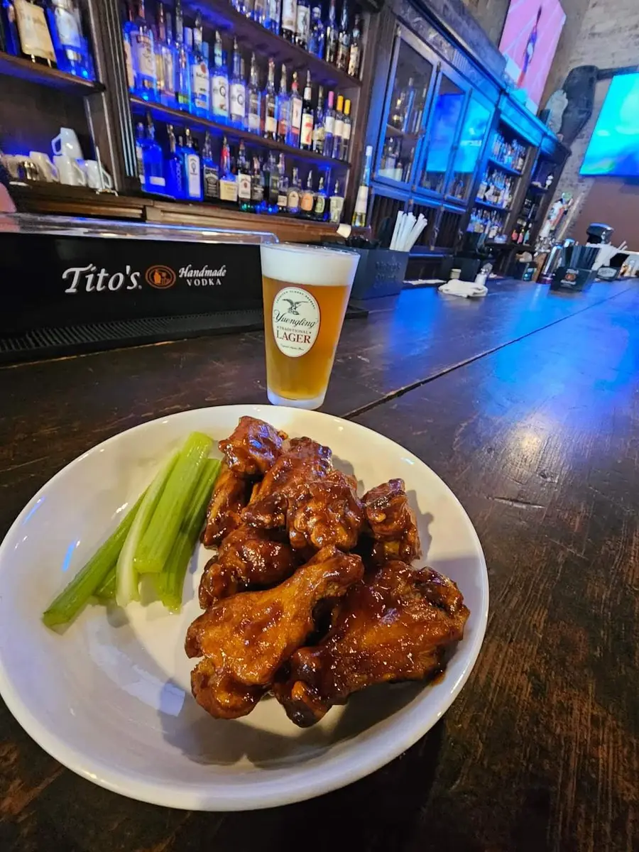 A plate of barbecue glazed wings with celery and a cold draft lager on the bar at Old Towne Pub