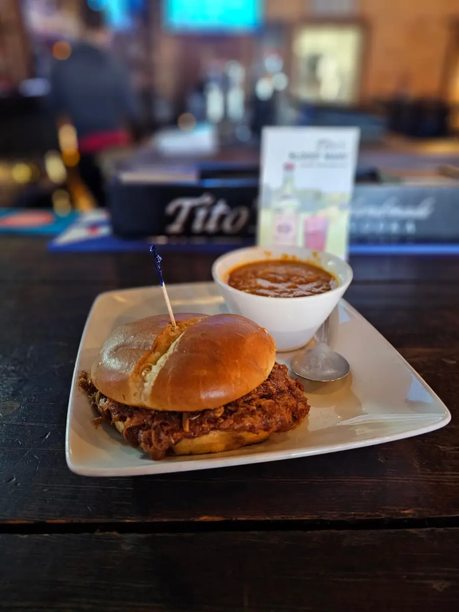 A pulled pork sandwich on a brioche bun with a cup of chili on the side